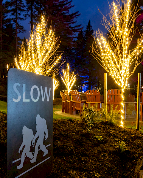 At night, a &ldquo;SLOW&rdquo; sign stands beside glowing light-wrapped trees and rows of chairs in a garden event area.