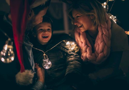 A joyful group of people, including a child, are surrounded by festive lights, creating a warm, happy atmosphere.
