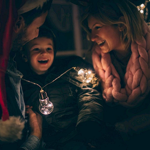 A joyful group of people, including a child, are surrounded by festive lights, creating a warm, happy atmosphere.