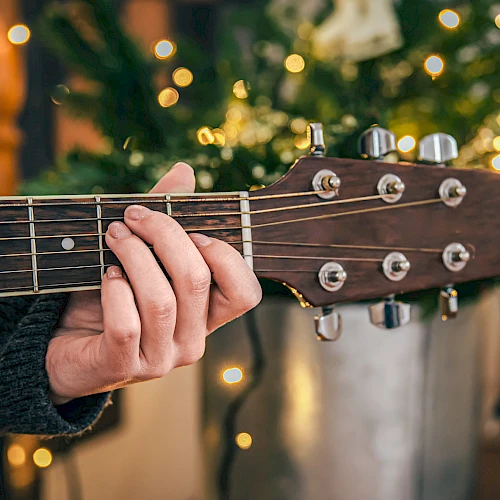 A person is playing an acoustic guitar, with a decorated Christmas tree in the background.