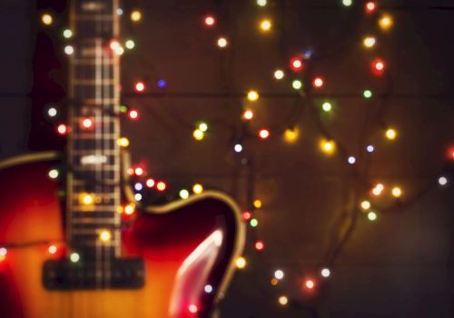 A close-up of a guitar with colorful string lights in the background creates a festive and artistic atmosphere.