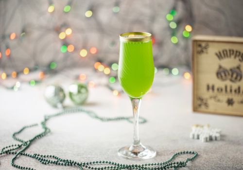 A festive scene with a green drink in a glass, holiday lights in the background, and a "Happy Holidays" sign.