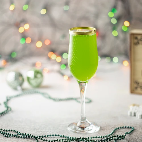 A festive scene with a green drink in a glass, holiday lights in the background, and a "Happy Holidays" sign.