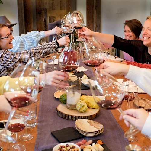 A group of people is toasting with glasses of red wine at a table with food and appetizers, sharing a joyful moment together.