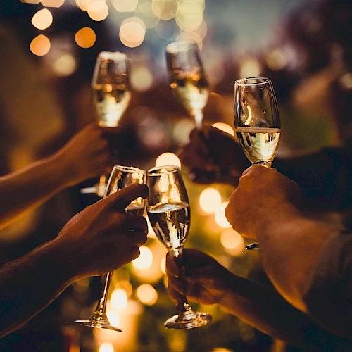 People are raising champagne glasses in a celebratory toast, with warm lighting and blurred bokeh in the background.