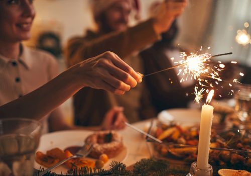 A festive dining scene with people holding sparklers at a table set with food and a lit candle.