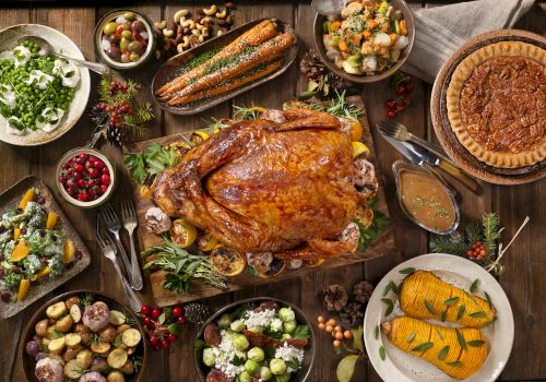 A Thanksgiving feast with roasted turkey, vegetables, stuffing, cranberries, pie, and various side dishes arranged on a wooden table.