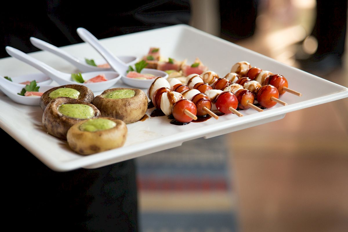 A platter with stuffed mushrooms, tomato and mozzarella skewers, and small dishes with diced vegetables.
