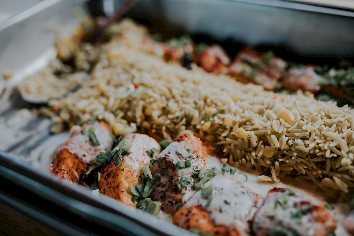 The image shows a tray with seasoned chicken pieces topped with creamy sauce and garnished with herbs, accompanied by a serving of rice.