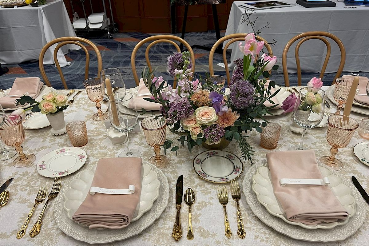 A beautifully set table with elegant dinnerware, pastel napkins, floral centerpieces, and ornate gold cutlery, perfect for a sophisticated gathering.