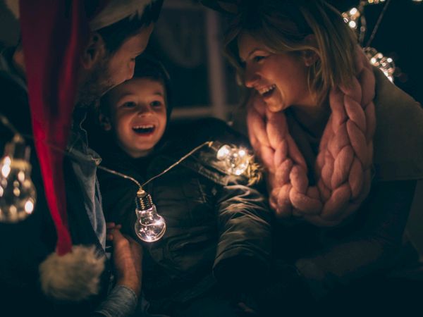 A joyful child and adult share a festive moment, smiling under holiday lights and a string of glowing bulbs.