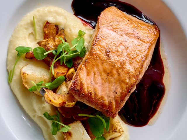 Pan-seared salmon over creamy puree with sautéed mushrooms and greens, plated with a dark berry reduction sauce on the side.