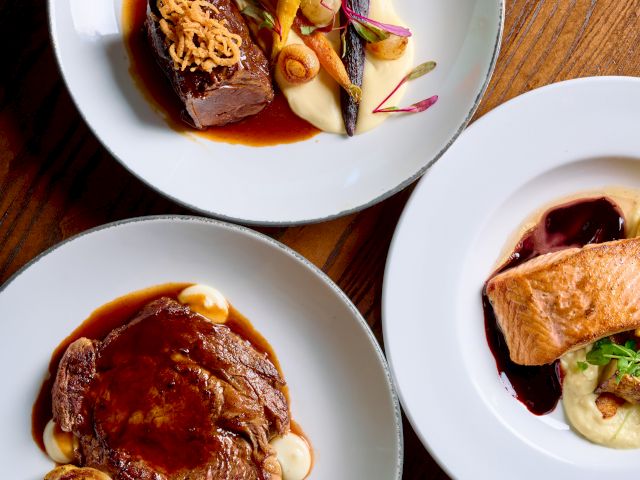 A trio of elegant plated dishes: a seared meat with sauce and vegetables, another meat dish with roots, and a pâté or crusted item with garnishes, all on white plates.