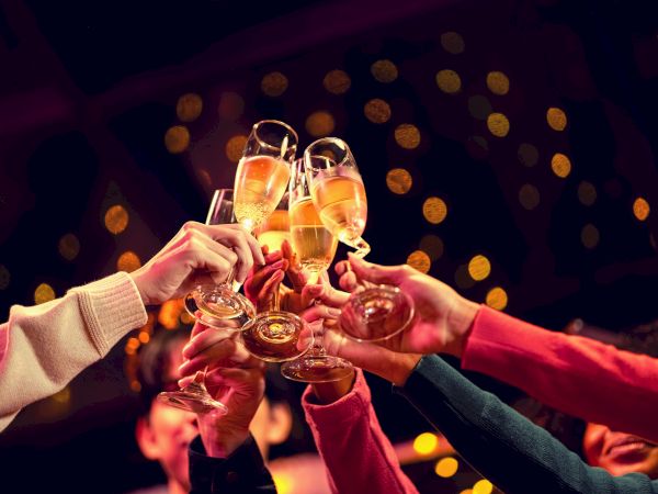 Friends raise champagne glasses in a toast, celebration vibe with warm bokeh lights in the background.