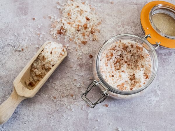 It shows a jar of brown sugar with a scoop and loose sugar spilled around it, on a marble-like surface.