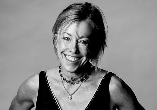 A smiling woman with short hair in a sleeveless top, necklace, and a confident pose.