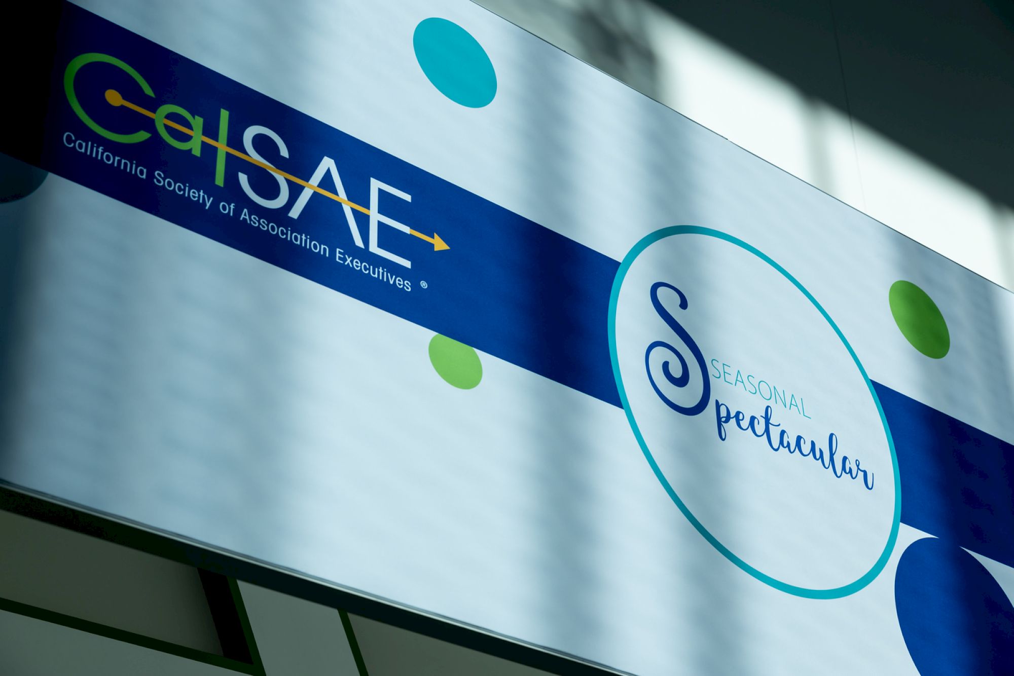 A banner showing “CalSAGE” and a circular logo with “Spectacular” text, plus colorful dots and a blue stripe across the sign.