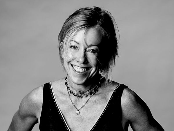 A smiling woman with a sleeveless top and layered necklaces, posing confidently in a black-and-white portrait.