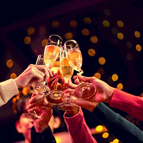 People clinking champagne flutes in a festive toast at a party, with warm bokeh lights in the background.