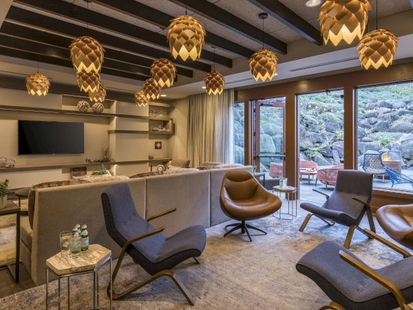 Cozy, modern lounge with mid-century chairs, a long counter, warm pendant lights, large windows to an outdoor deck, and a calm, inviting vibe.