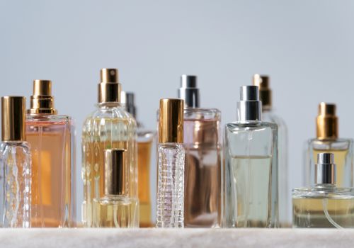 A row of assorted perfume bottles with spray tops in gold, silver, and clear glass, arranged on a light surface.