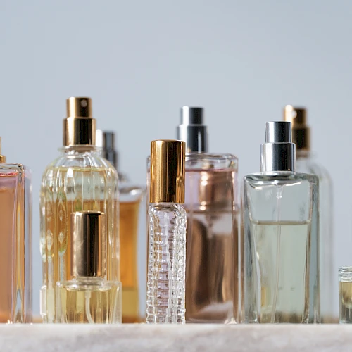 A row of assorted perfume bottles with spray tops in gold, silver, and clear glass, arranged on a light surface.