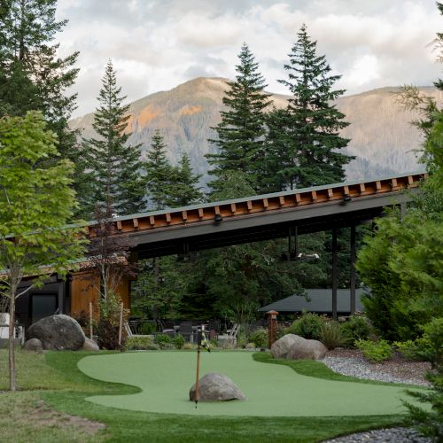 A landscaped area with a sloping roof structure, surrounded by trees and mountains in the background, with a green and rocks in the foreground.