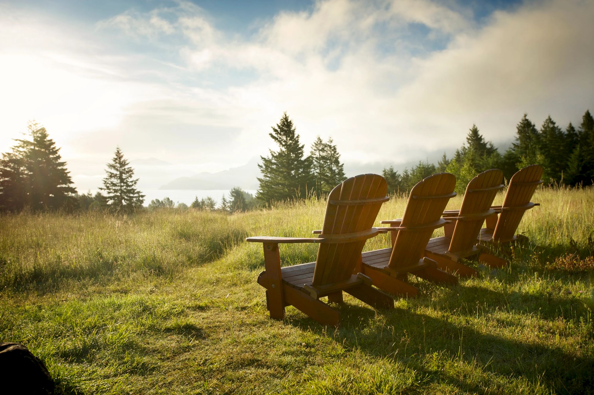 Wooden chairs face a scenic view with trees, grass, and a cloudy sky, creating a peaceful and tranquil outdoor setting.