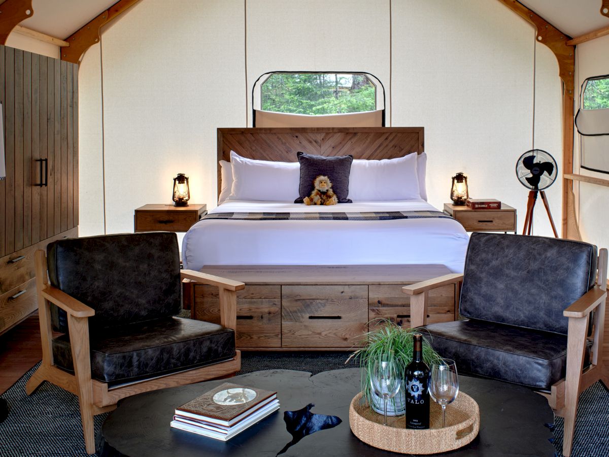 A luxurious hotel tent bedroom with a king bed, wooden furniture, two armchairs, a round coffee table, and tasteful lighting. Ending sentence.