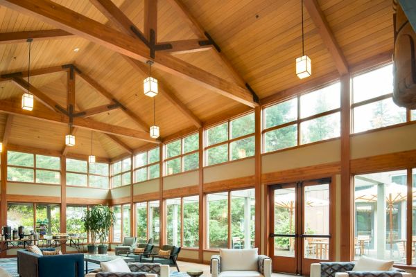 A spacious lounge with a wooden ceiling, large windows, modern furniture, and warm lighting creates a cozy and inviting atmosphere.