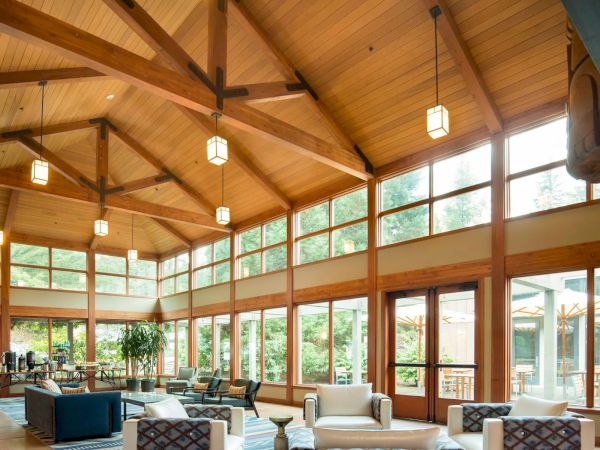 A spacious lounge with a wooden ceiling, large windows, modern furniture, and warm lighting creates a cozy and inviting atmosphere.