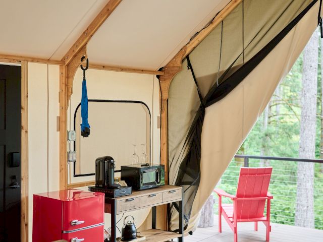 Wood-paneled cabin interior with a small kitchen, red fridge, hanging string lights, and an open patio view through large windows.