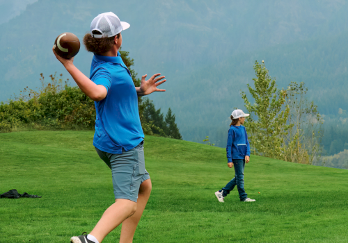 A woman and child in blue play football on a grassy field with mountains in the background.