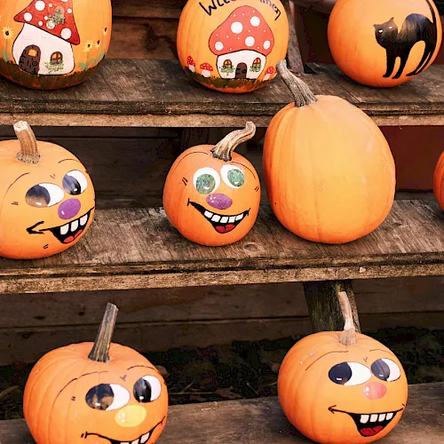 Colorful cartoon pumpkins with funny faces, some wearing hats, lined up on rustic wooden shelves for Halloween.