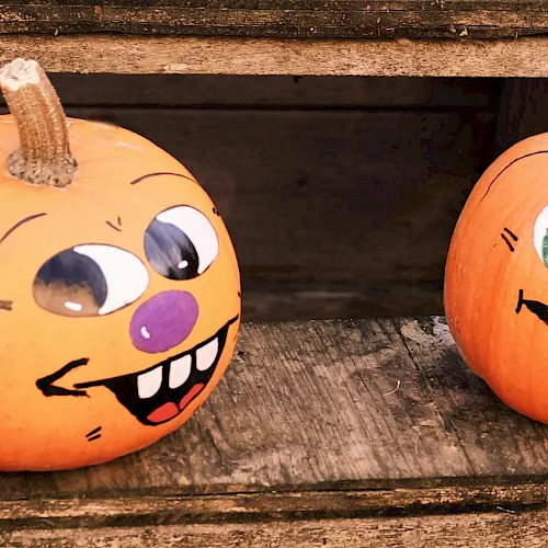 Two Halloween pumpkins carved with silly faces sit on a wooden surface, one with a stem and the other smiling wide.