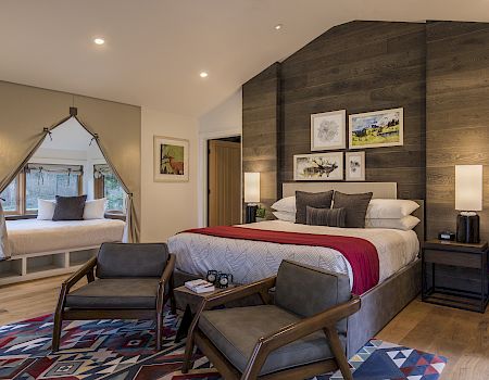 A modern bedroom with a wood-paneled accent wall, framed art, lamps, and a made bed with pillows.