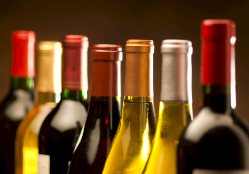 A lineup of wine bottles with colorful labels and warm, blurred background lighting.