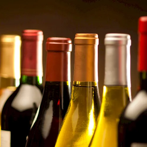 A lineup of wine bottles with colorful labels and warm, blurred background lighting.