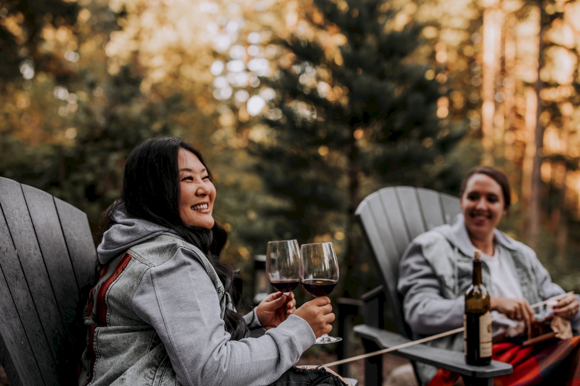 Two people relax outdoors at a table, smiling and toasting with wine glasses in a golden autumn setting.
