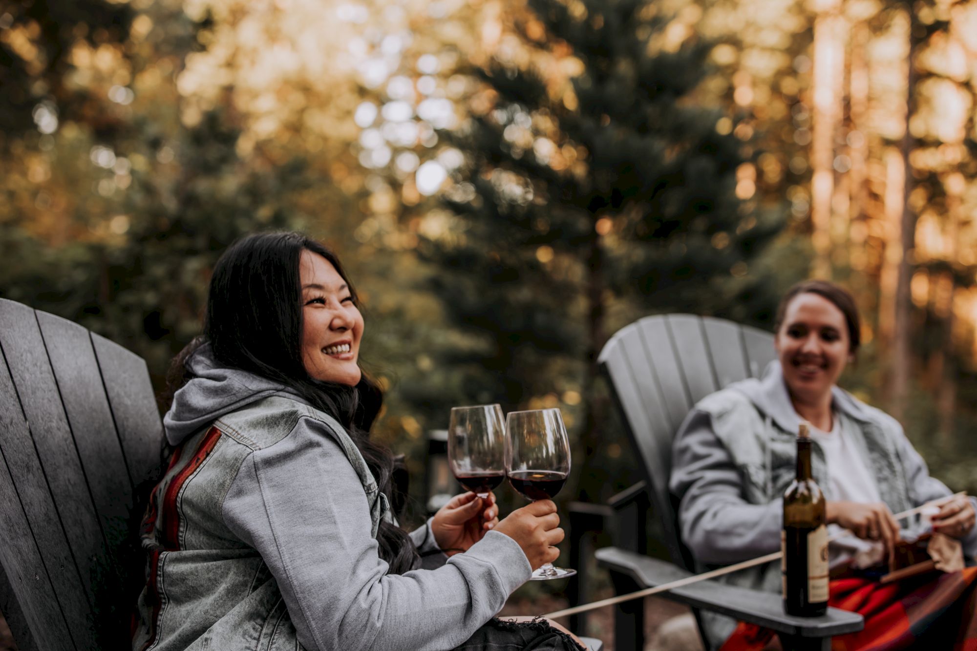 Two people relax outdoors at a table, smiling and toasting with wine glasses in a golden autumn setting.