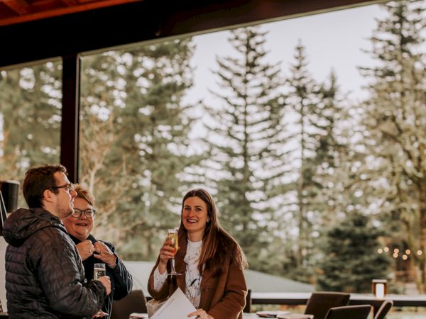 Friends toast with drinks at a cozy outdoor caf&eacute; under a wooden pavilion with string lights.