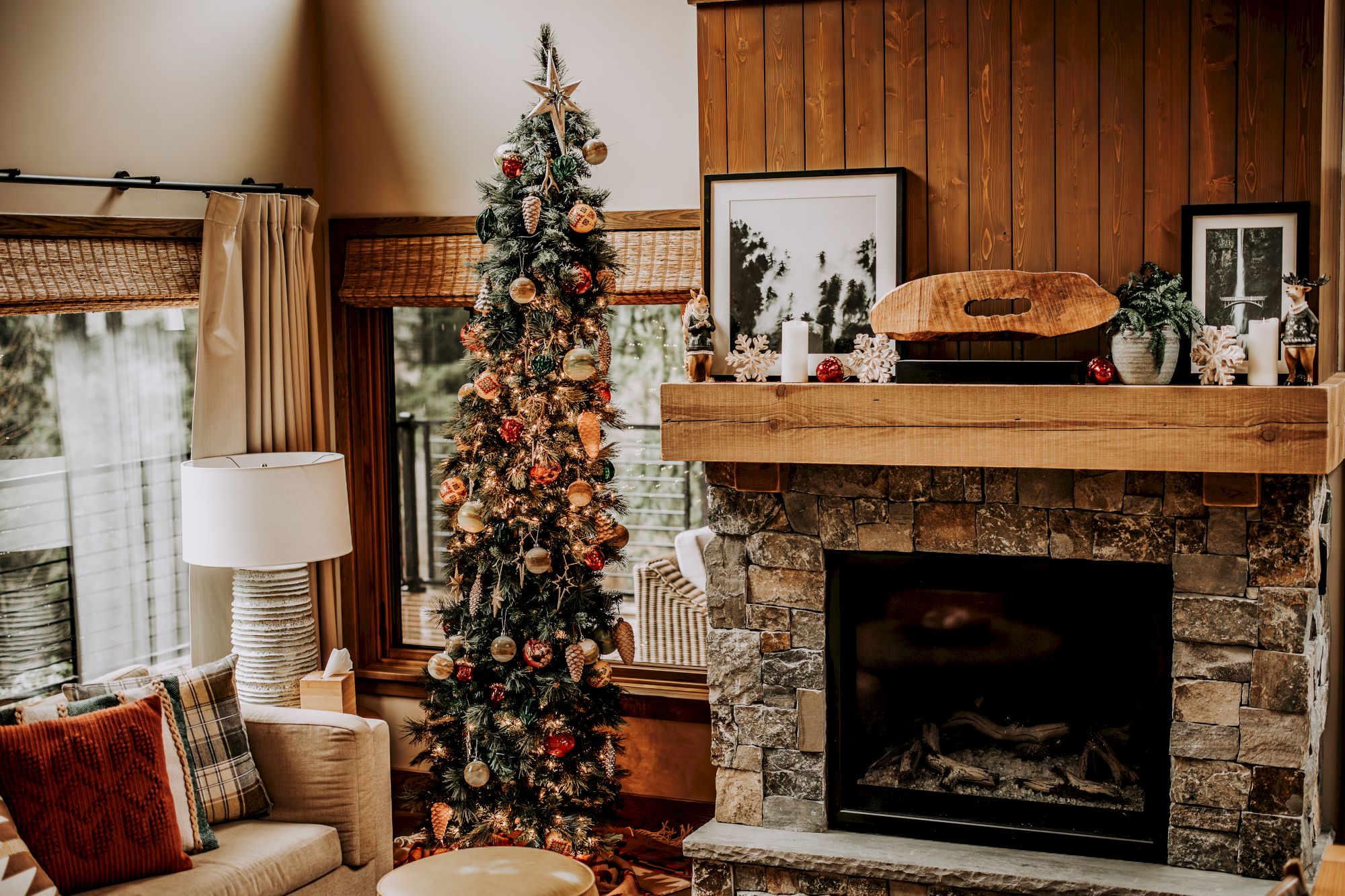 A decorated Christmas tree stands by a stone fireplace and festive mantel in a cozy living room.