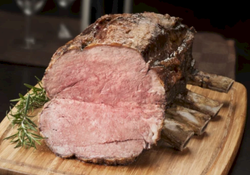 A sliced roast ham with a browned crust on a wooden cutting board, garnished with fresh rosemary sprigs.
