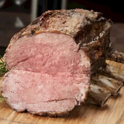 A sliced roast ham with a browned crust on a wooden cutting board, garnished with fresh rosemary sprigs.