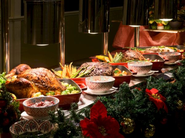 A festive buffet table with roasted chicken and vegetables, bowls, and holiday greenery under warm lights.
