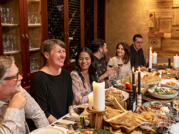 A cozy dinner party with friends laughing around a candlelit table, wine glasses in hand and lots of food on platters.