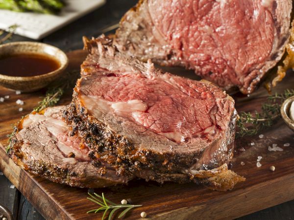 Juicy grilled steak on a wooden board, sliced and topped with herbs, sea salt, and a little butter sauce.