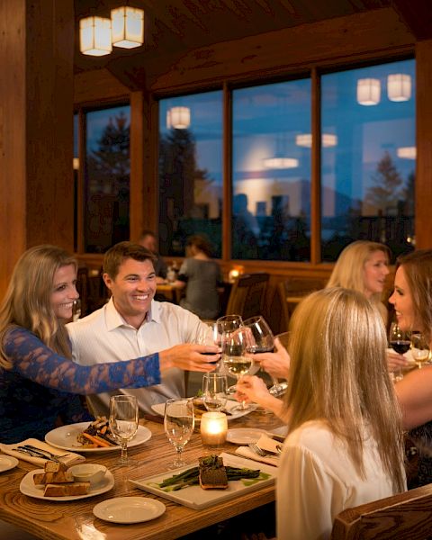 A group of friends cheers with wine glasses while dining together in a cozy, wood-paneled restaurant.