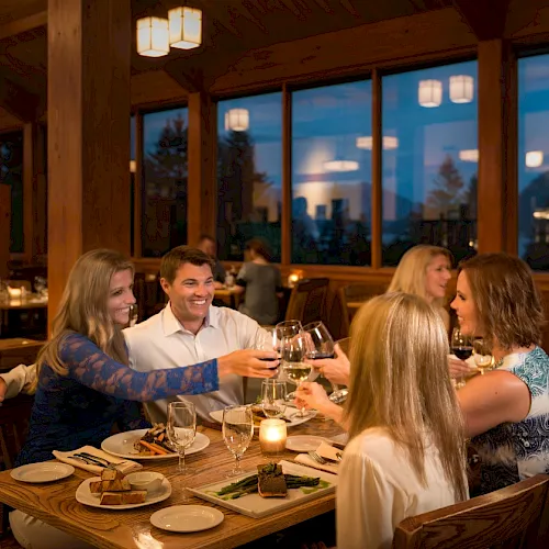 A group of friends cheers with wine glasses while dining together in a cozy, wood-paneled restaurant.