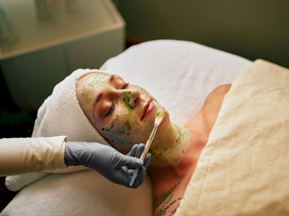 A clinician applies a green solution to a person&rsquo;s face during a skincare/cosmetic treatment on a treatment bed.